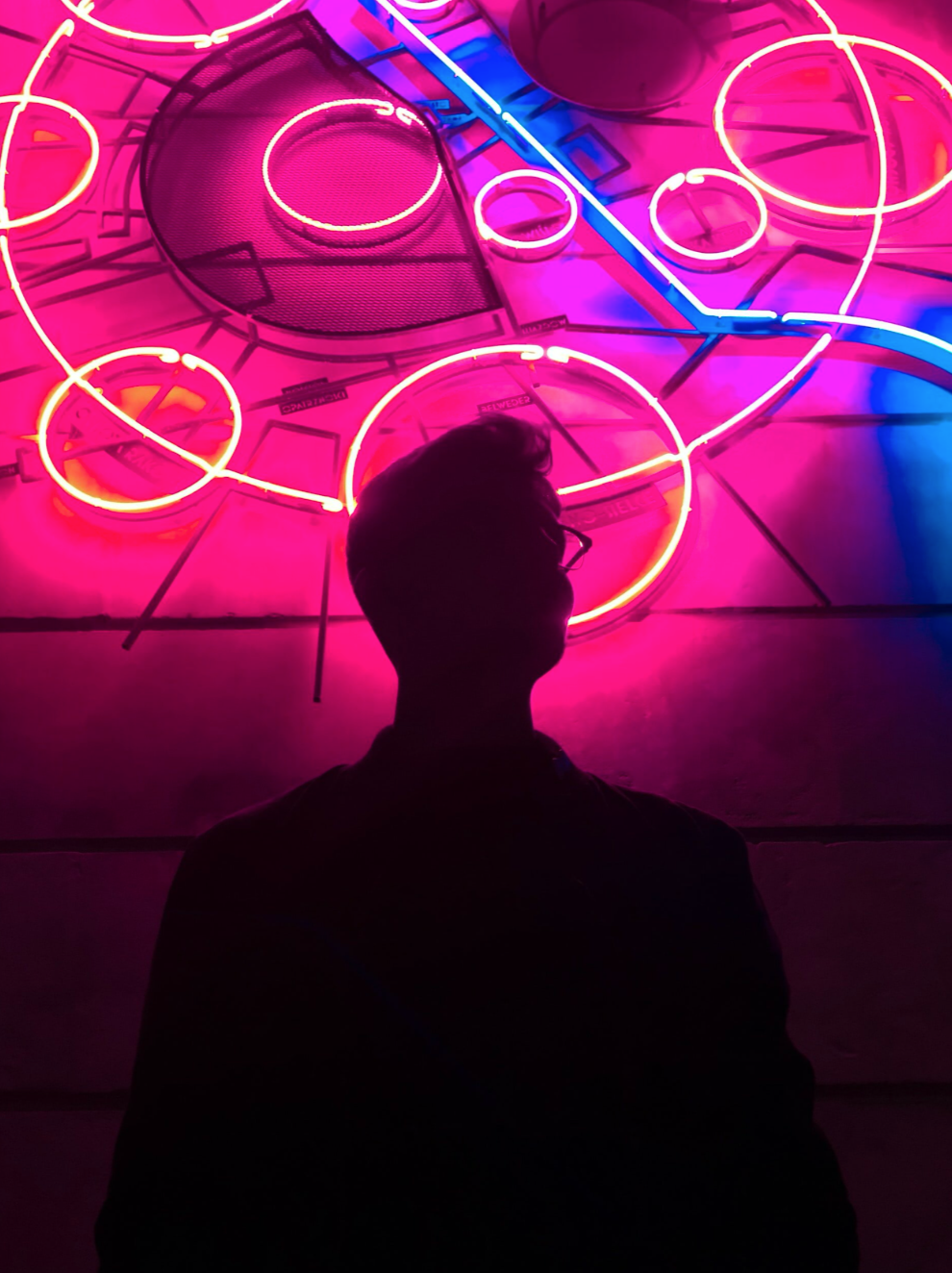 person with glasses in front of neon sign on wall