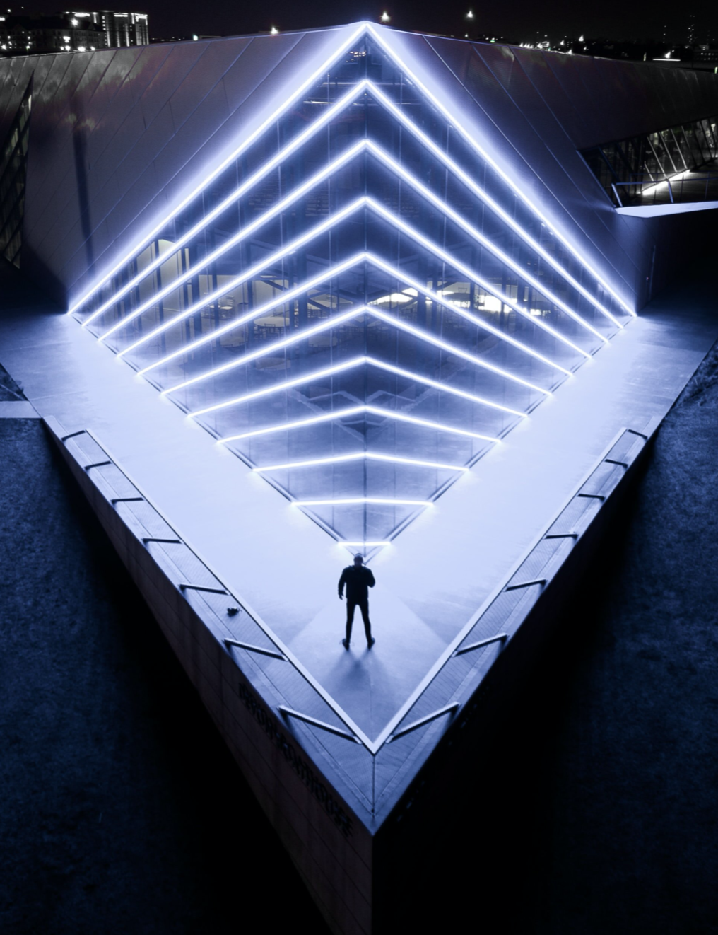 person in front of large neon sculpture pyramid