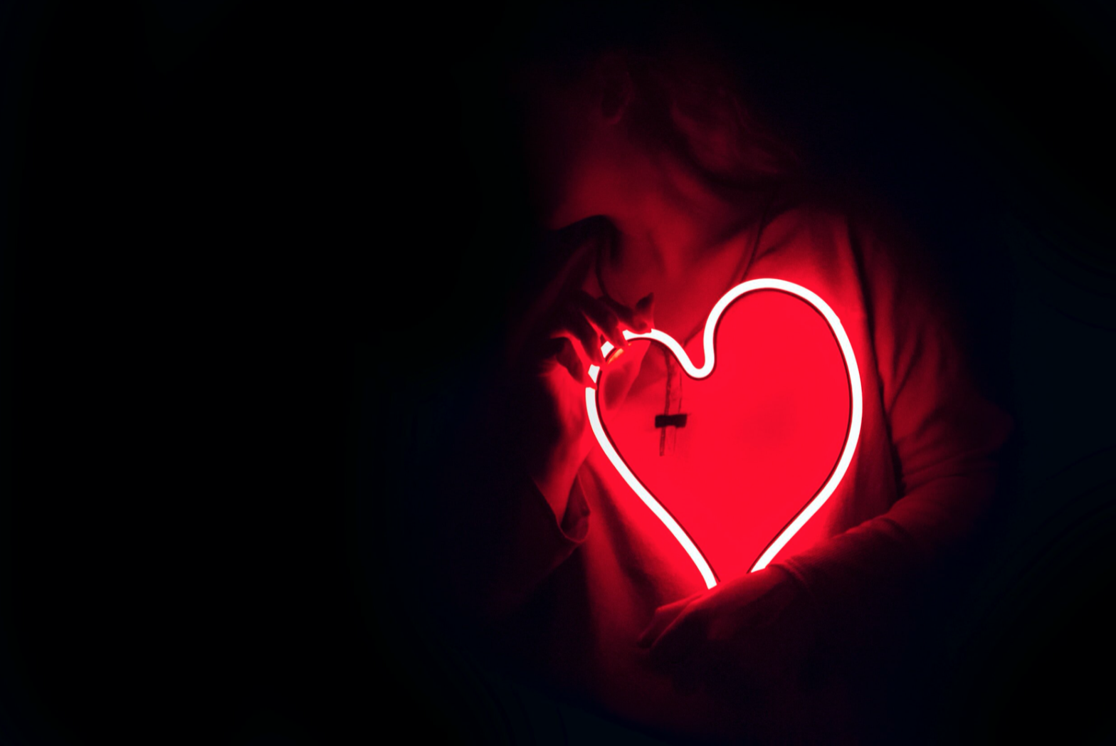 red neon heart sign being held by woman